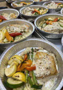 Individual dinners for disposable drop-off catering served in round aluminum tins with sea bass, roasted vegetables, and mushroom risotto