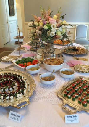 Private event catering display in a home's dining room featuring a table with an array of DailyDish hors d'oeuvres, including caprese skewers, sesame seared ahi tuna, and hummus with vegetables and crackers