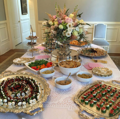 Private event catering display in a home's dining room featuring a table with an array of DailyDish hors d'oeuvres, including caprese skewers, sesame seared ahi tuna, and hummus with vegetables and crackers {{brizy_dc_image_alt imageSrc=