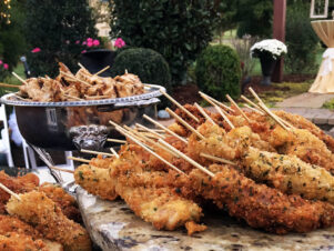 A silver serving dish with pork satay skewers next to a marble slab with coconut chicken satay skewers, set for an outdoor private event catered by DailyDish Events & Catering, Franklin TN