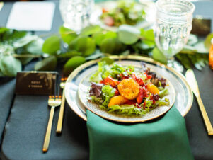DailyDish's most popular salad, the strawberry salad served with a coconut goat cheese cake and raspberry vinaigrette, plated on gold-rimmed china with an emerald green napkin, gold flatware, and black tablecloth. Catering Franklin TN