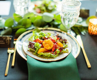 DailyDish's most popular salad, the strawberry salad served with a coconut goat cheese cake and raspberry vinaigrette, plated on gold-rimmed china with an emerald green napkin, gold flatware, and black tablecloth. Catering Franklin TN