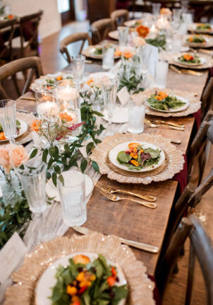 A rustic wedding table set with ornate gold chargers with gold-rimmed china featuring our strawberry salad