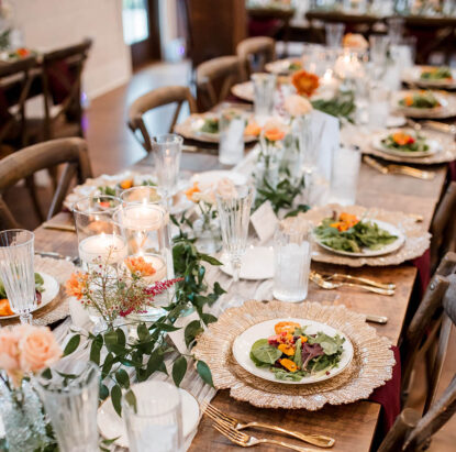 A rustic wedding table set with ornate gold chargers with gold-rimmed china featuring our strawberry salad